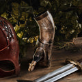 Decorative horn, leather helmet, and sword on a wooden surface with green foliage in the background