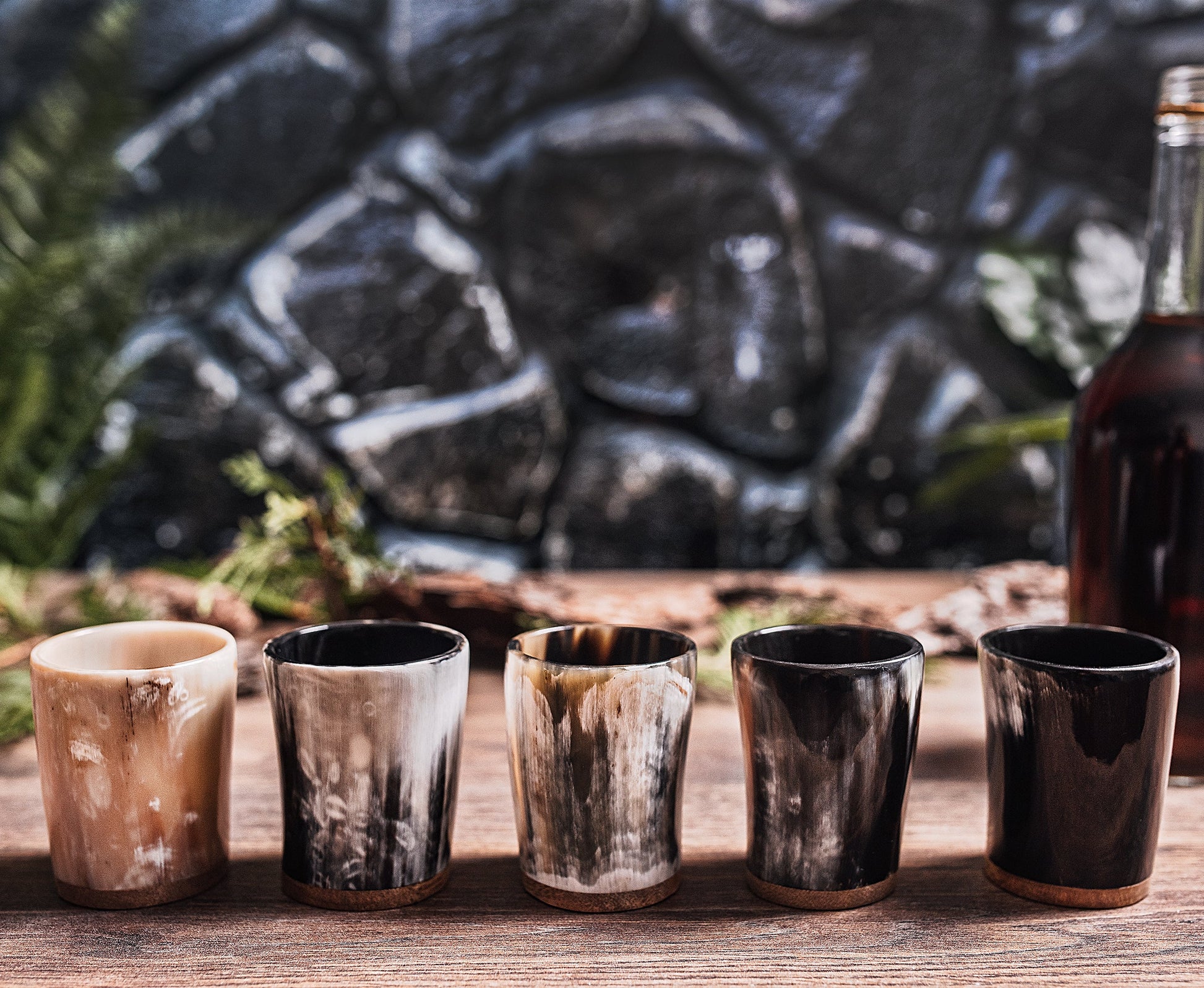 Set of five wooden shot glasses on a wooden surface with a stone wall background