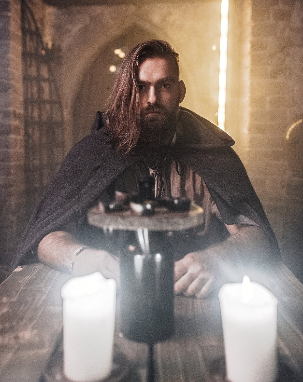 Man in a dark robe with candles in a dimly lit room