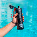 RIPTIDE The Shotgun Bottle held over a pool, showcasing its sleek design and water-resistant features.