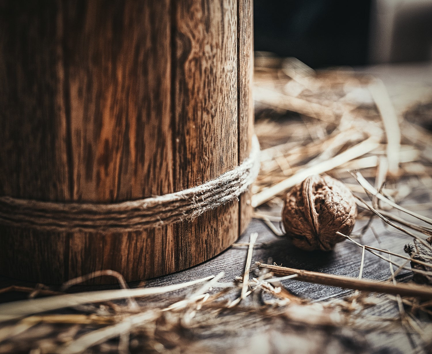 Close-up of a wooden container with twine, surrounded by straw and wood chips on a dark surface.
