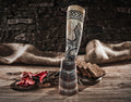 Decorative horn with carvings on a wooden surface with food items and a stone wall background