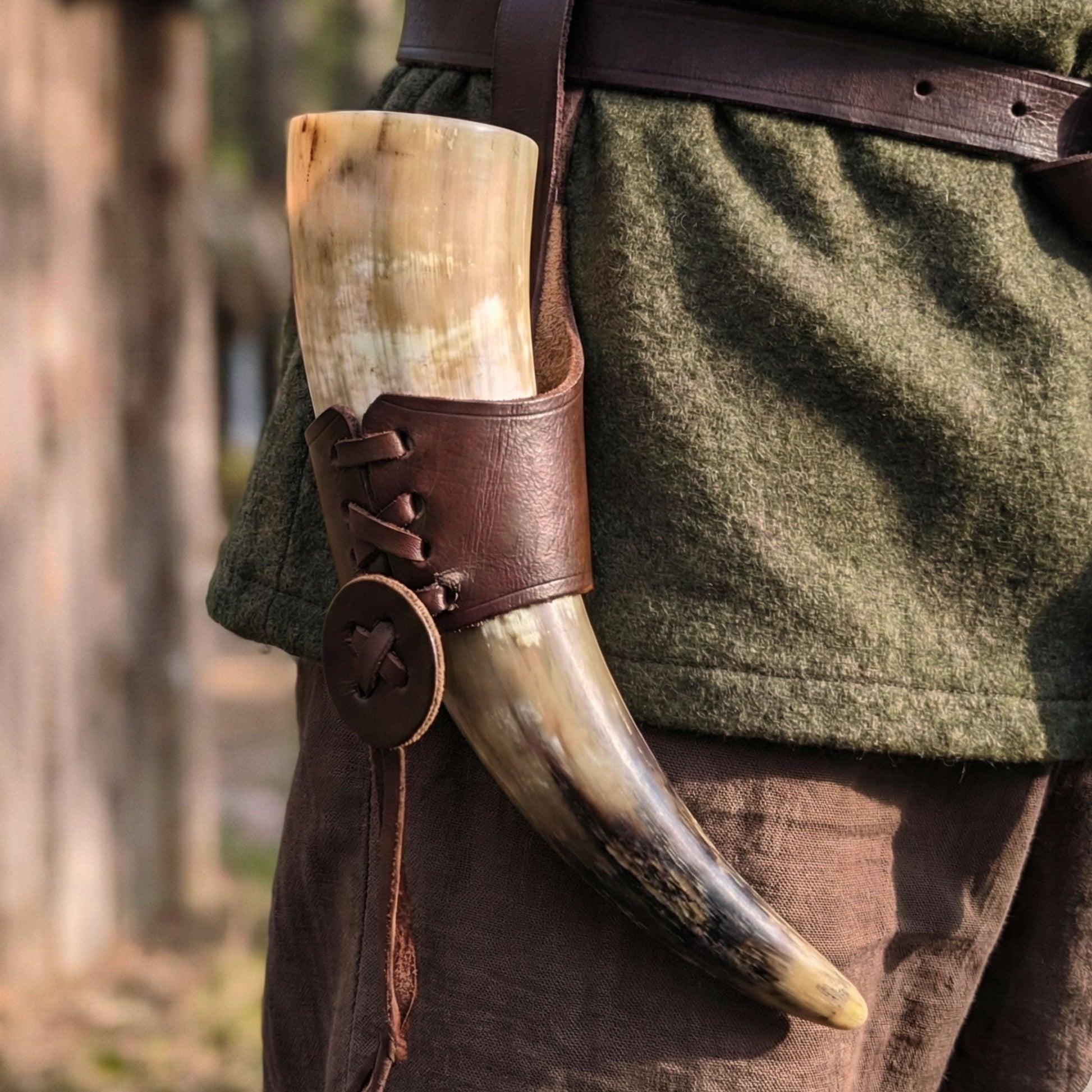 Tusk in a leather holder on a person wearing green fabric and brown leather belt outdoors.