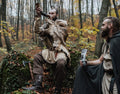 Two men in medieval or fantasy costumes sitting in a forest, one taking a selfie.