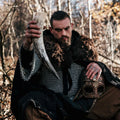 Man in medieval attire holding a large tusk and a helmet in a forest setting