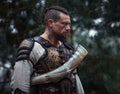 Man in Viking armor holding a horn against a forest background