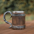 Wooden mug with metal handle and band on a wooden surface with blurred greenery in the background