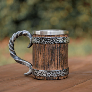 Wooden mug with metal handle and band on a wooden surface with blurred greenery in the background