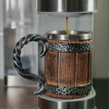 Wooden mug with metal handle and base, filled with coffee being poured.