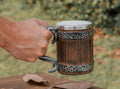 Wooden mug with metal handle and rim held by a hand against a natural background