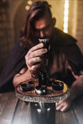 Person holding a small bottle over a wooden tray with other bottles on a rustic setting