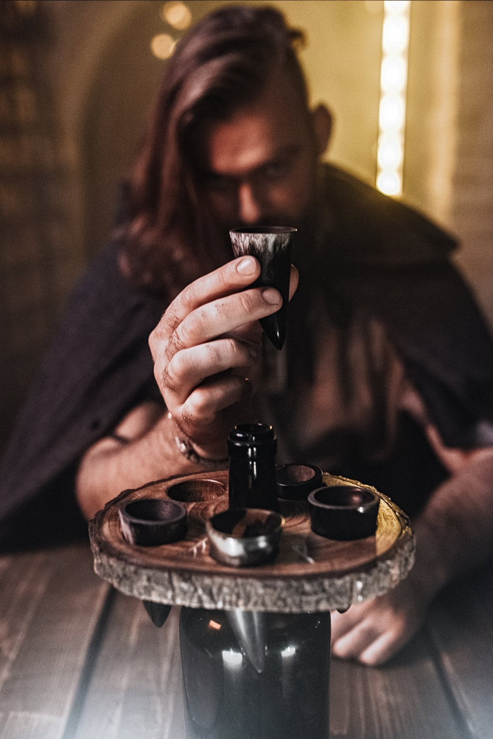 Person holding a small bottle over a wooden tray with other bottles on a rustic setting